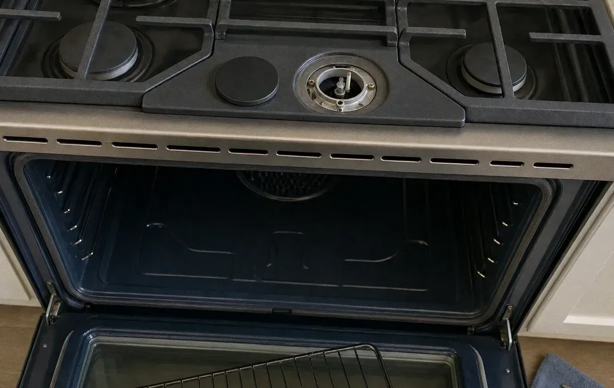 Cast-iron grates on a rangetop with one burner base exposed and the oven door open below